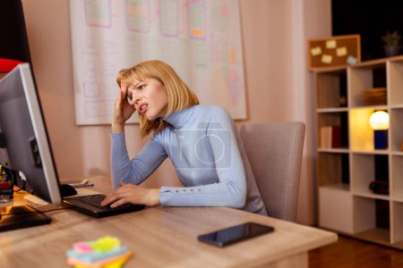 Woman working in an office sitting at her desk stressed out and exhausted while working overtime to meet a project deadline