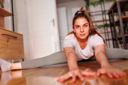 Téléchargez les photos : Jeune femme active en tenue de sport s'étirant sur un tapis de yoga et se réchauffant pour une séance d'entraînement à la maison - en image libre de droit