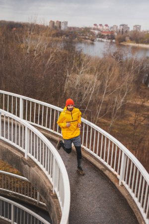 Foto de Vista de ángulo alto de un hombre activo corriendo en la ruta del puente como parte de la rutina diaria de entrenamiento matutino en un día nublado lluvioso - Imagen libre de derechos