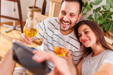 Téléchargez les photos : Jeune couple amoureux déménager dans un nouvel appartement, faire un toast boire du vin et s'amuser à prendre des selfies - en image libre de droit