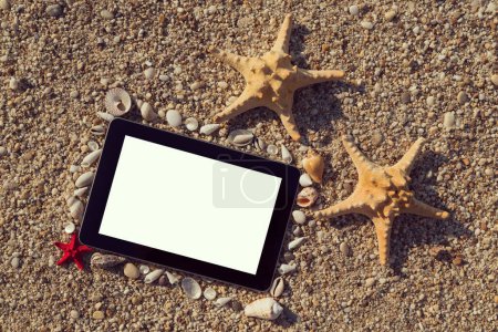 Photo for Photo frame made of seashells and pebbles with two starfish placed next to it and tablet computer within the frame with blank screen on the beach - Royalty Free Image