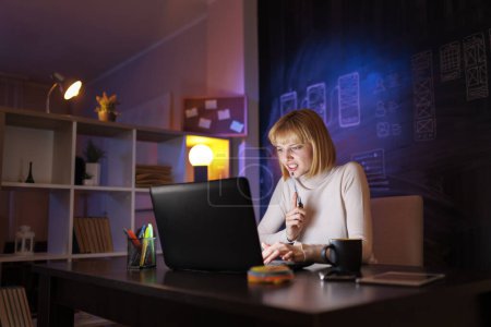 Téléchargez les photos : Femme assise à son bureau à la maison, écrivant dans le planificateur tout en ayant une réunion en ligne - en image libre de droit