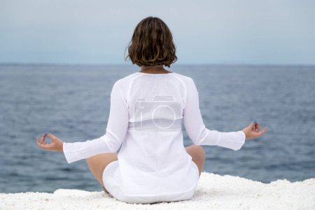 Téléchargez les photos : Jeune femme pratiquant le yoga près de la plage de marbre sur l'île de Thassos, Grèce par une journée d'été nuageuse - en image libre de droit