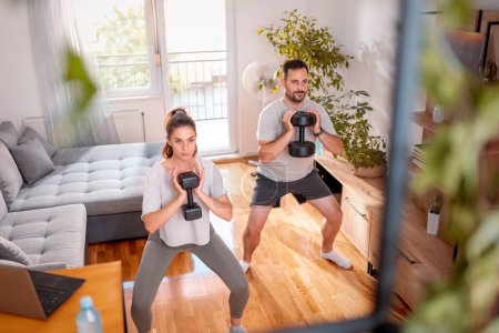 Téléchargez les photos : Couple travaillant à la maison faisant squats à l'aide d'haltères - en image libre de droit