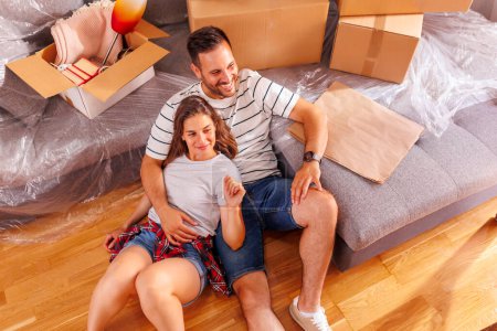 Téléchargez les photos : Vue en angle élevé du jeune couple amoureux couché sur le sol de leur nouvelle maison, étreignant et relaxant, prenant une pause tout en emménageant ensemble - en image libre de droit