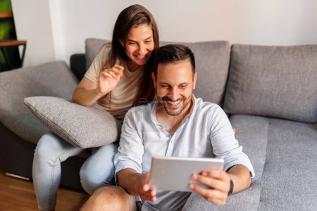 Téléchargez les photos : Beau jeune couple amoureux se détendre à la maison, surfer sur Internet à l'aide d'une tablette - en image libre de droit