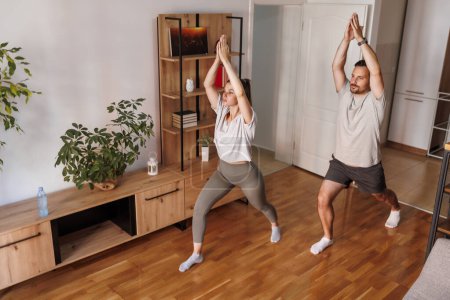 Foto de Pareja joven haciendo ejercicio juntos en casa, haciendo yoga como rutina de ejercicios matutinos - Imagen libre de derechos
