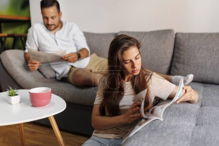 Téléchargez les photos : Couple lire le journal et le magazine et boire du café tout en passant du temps libre ensemble à la maison - en image libre de droit