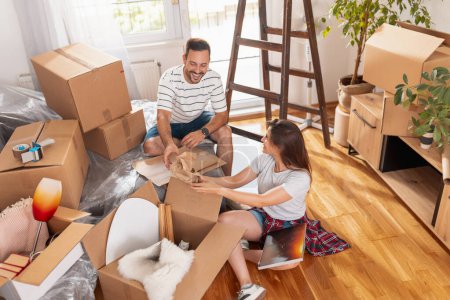 Photo for Beautiful young couple in love having fun unpacking things from cardboard boxes while moving in together in their new house - Royalty Free Image