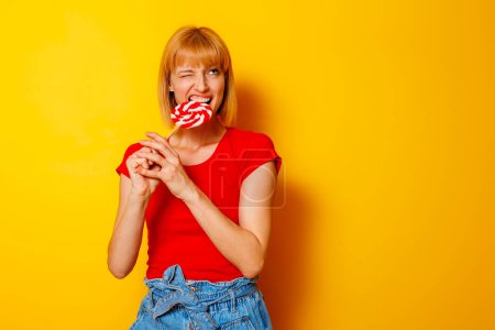 Foto de Hermosa mujer rubia en verano de moda usar dulces mordedoras y hacer caras divertidas en el fondo de color amarillo con espacio de copia - Imagen libre de derechos