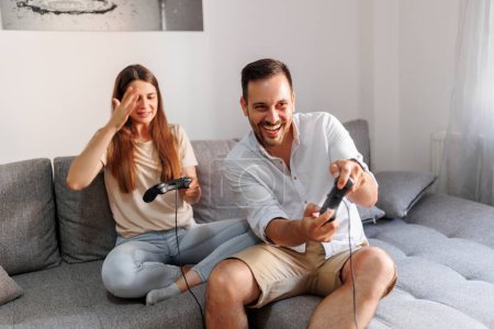 Téléchargez les photos : Couple joyeux en amour s'amuser à jouer à des jeux vidéo tout en passant du temps libre ensemble à la maison - en image libre de droit