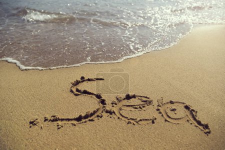 Téléchargez les photos : Mot mer écrit à la main dans le sable sur la plage à côté de la ligne de flottaison - en image libre de droit