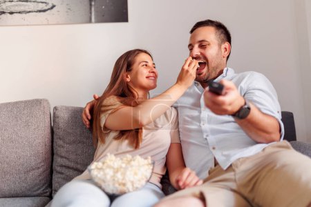 Photo for Couple in love spending leisure time together at home, having fun watching TV and eating popcorn, binging TV shows on weekend - Royalty Free Image