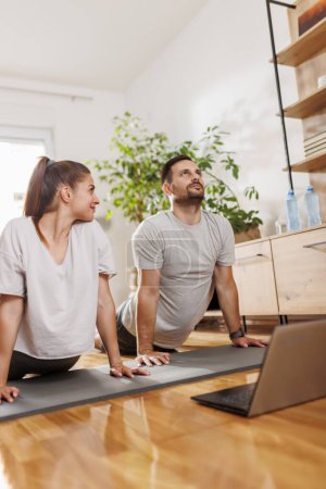 Téléchargez les photos : Couple travaillant ensemble à la maison, se détendre tout en faisant un cours de yoga en ligne comme routine d'exercice du matin - en image libre de droit