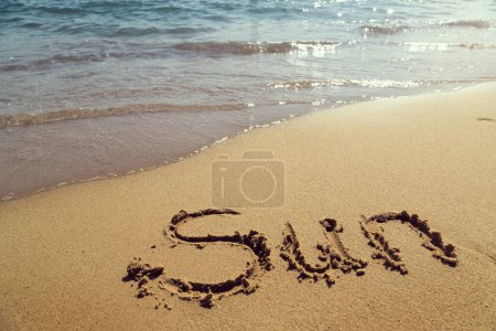 Téléchargez les photos : Mot soleil écrit à la main sur le sable sur la plage à côté de la ligne d'eau - en image libre de droit