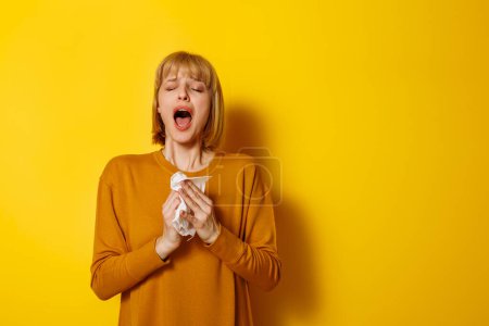 Foto de Retrato de mujer enferma estornudando y sonándose la nariz mientras tiene gripe aislada sobre fondo de color amarillo con espacio para copiar - Imagen libre de derechos