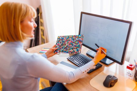 Téléchargez les photos : Designer féminin travaillant à distance de la maison, en utilisant la palette de couleurs et le tampon de dessin tout en travaillant dans le bureau à domicile - en image libre de droit