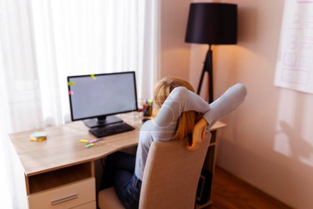 Foto de Mujer estirándose mientras está sentada en su escritorio en la oficina del hogar, cansada mientras trabaja horas extras - Imagen libre de derechos