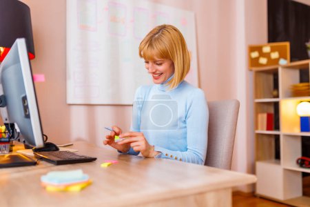 Téléchargez les photos : Femme assise à son bureau au bureau à la maison, prenant des notes tout en faisant du remue-méninges à la recherche d'idées et d'inspiration - en image libre de droit