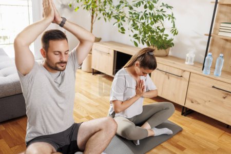 Photo for Couple relaxing while doing yoga as morning exercise routine together at home - Royalty Free Image
