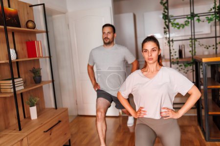 Photo for Active young couple stretching after working out together at home - Royalty Free Image