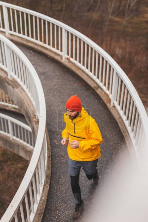 Photo for High angle view of an active man jogging on the bridge pathway as part of daily morning workout routine on a rainy cloudy day - Royalty Free Image