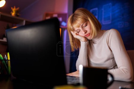 Téléchargez les photos : Femme assise à son bureau à la maison, fatiguée en faisant des heures supplémentaires, s'appuyant sur sa main et dormant - en image libre de droit
