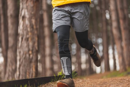 Téléchargez les photos : Détail d'un homme actif faisant du jogging dans le parc le matin par une journée d'automne nuageuse - en image libre de droit