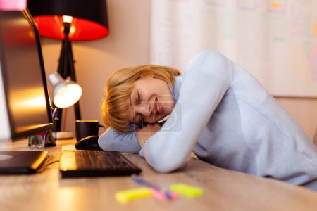 Téléchargez les photos : Femme assise à son bureau à la maison, fatiguée en faisant des heures supplémentaires, s'appuyant sur son bureau et dormant - en image libre de droit