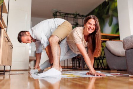 Photo for Cheerful young couple in love having fun spending leisure time together at home playing games, bending and keeping balance while holding unusual positions - Royalty Free Image