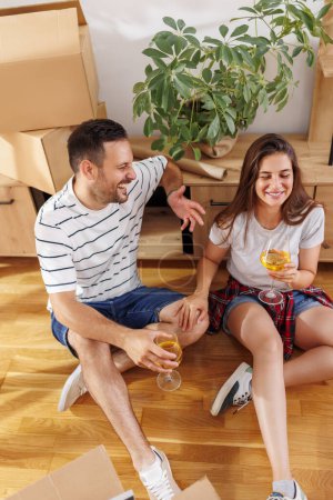 Photo for High angle view of beautiful young couple in love celebrating moving in new home, drinking wine, laughing and having fun - Royalty Free Image