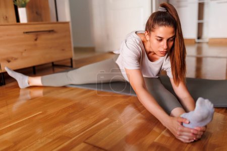 Téléchargez les photos : Jeune femme en vêtements de sport étirant sur tapis de yoga après avoir fait de l'entraînement à la maison - en image libre de droit