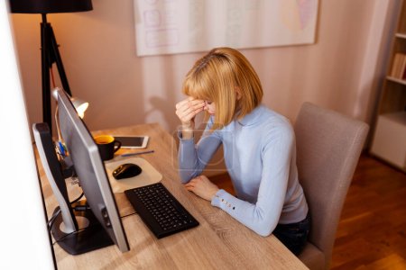 Woman working in an office, sitting at her desk, holding head in hands, having a headache