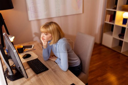 Mujer sentada en su escritorio, ansiosa mientras trabaja en una oficina usando una computadora de escritorio
