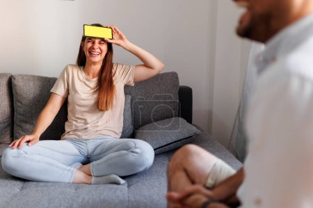 Téléchargez les photos : Couple s'amuser à la maison jouer des charades, expliquer et deviner les mots d'une application smartphone - en image libre de droit
