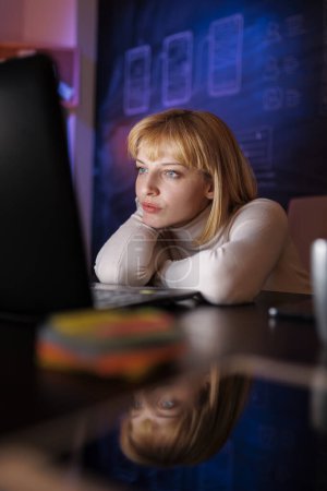 Foto de Mujer trabajando horas extras hasta tarde en la noche en la oficina en casa, cansada mientras está sentada en su escritorio y usando el ordenador portátil - Imagen libre de derechos