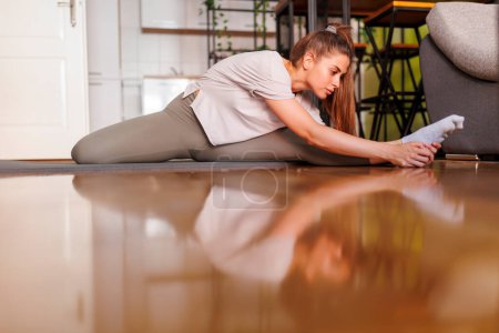 Téléchargez les photos : Vue à angle bas de la jeune femme en vêtements de sport étirant sur tapis de yoga après avoir fait de l'entraînement à la maison - en image libre de droit