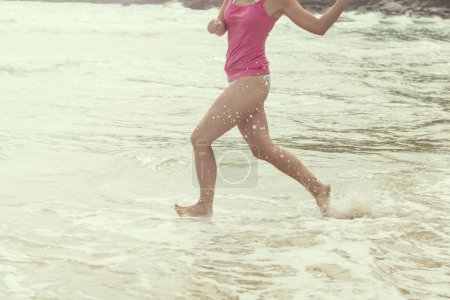 Young happy woman running through water and splashing it. Enjoyment and freedom on beach holidays