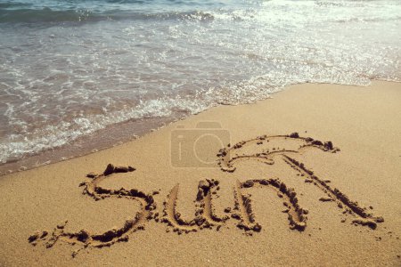 Téléchargez les photos : Mot soleil écrit à la main sur le sable sur la plage à côté de la ligne d'eau - en image libre de droit