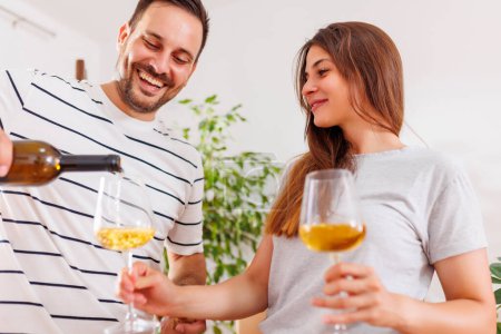 Téléchargez les photos : Beau jeune couple amoureux célébrant le déménagement dans un nouvel appartement ensemble, ouvrant une bouteille de vin et portant un toast - en image libre de droit