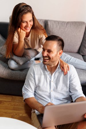 Téléchargez les photos : Couple amoureux passer du temps ensemble à la maison, surfer sur Internet à l'aide d'un ordinateur portable - en image libre de droit