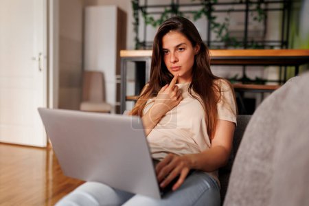 Foto de Hermosa mujer joven acostada en el sofá con el ordenador portátil en su regazo, tomando un curso en línea, aprendiendo en Internet - Imagen libre de derechos