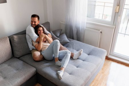 Téléchargez les photos : Beau jeune couple amoureux se détendre à la maison, couché et étreignant sur le canapé - en image libre de droit