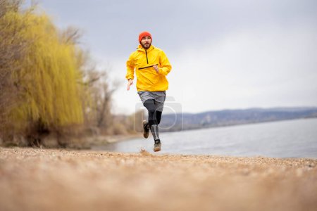 Téléchargez les photos : Homme athlétique allant pour une course matinale au bord de la rivière par une journée d'automne nuageuse - en image libre de droit