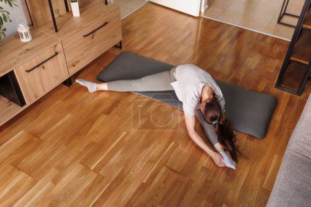 Foto de Vista de ángulo alto de la mujer joven en ropa deportiva que se extiende en la esterilla de yoga después de hacer ejercicio en casa - Imagen libre de derechos