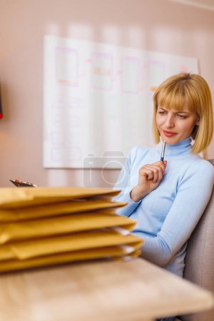 Photo for Small business owner sitting at her desk in home office, packing products for delivery; female entrepreneur packaging online store orders for shipping - Royalty Free Image