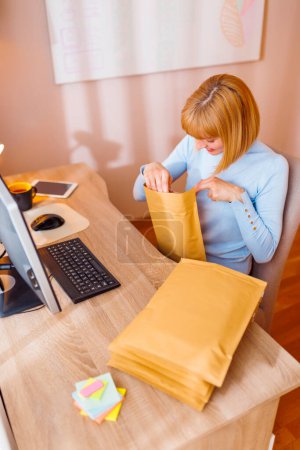 Photo for Woman small business owner sitting at her desk in home office, packing products for delivery; female entrepreneur packaging online store orders for shipping - Royalty Free Image