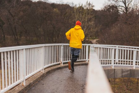 Téléchargez les photos : Homme actif courant sur le sentier du pont par une journée d'automne nuageuse - en image libre de droit