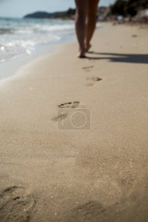 Téléchargez les photos : Femme marchant sur la plage, laissant des empreintes dans les cailloux - en image libre de droit