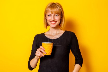 Foto de Retrato de una hermosa mujer rubia bebiendo café y sonriendo sobre fondo de color amarillo - Imagen libre de derechos
